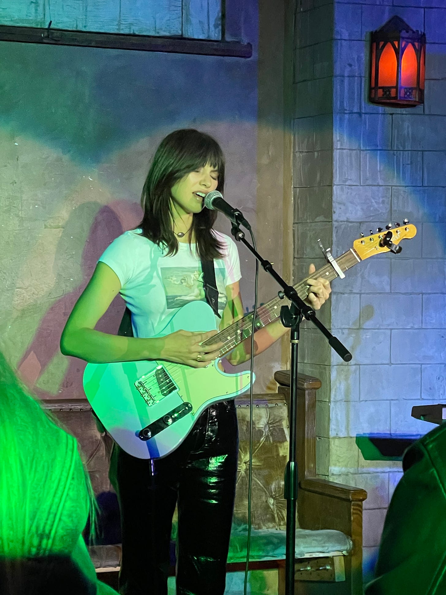 Alexandra Cadiz / Sette on stage playing the guitar and singing into a microphone.