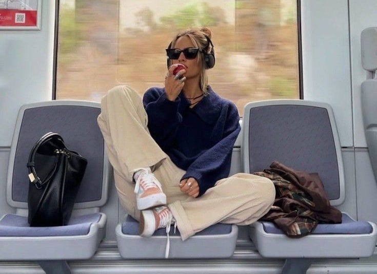 This may contain: a woman with headphones sitting on a train seat next to a handbag and purse