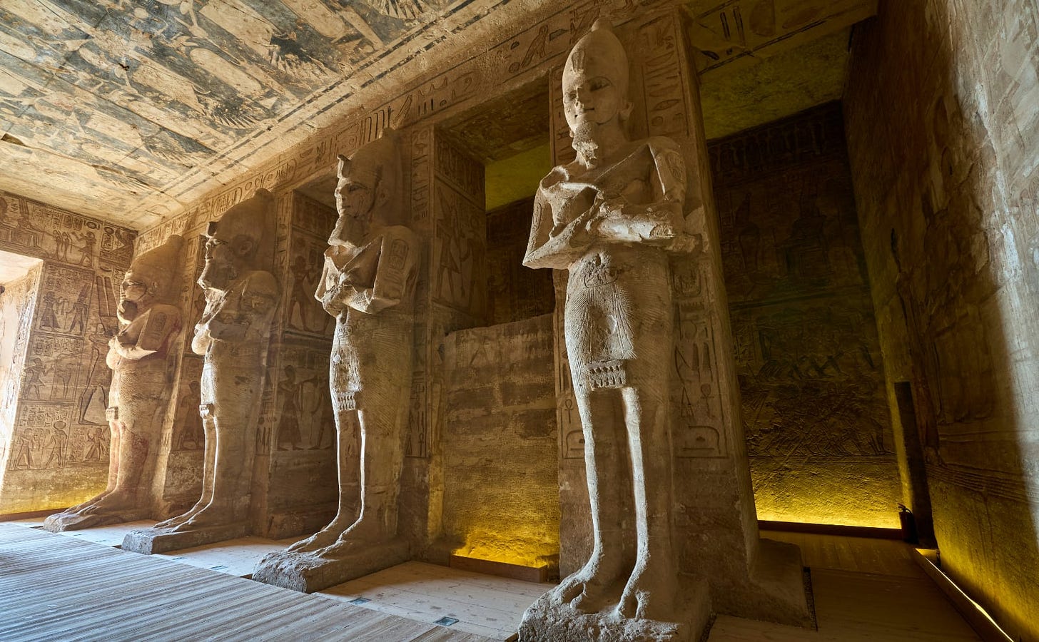 four tall sandstone egyptian statues in a hallway lit with bright sunlight