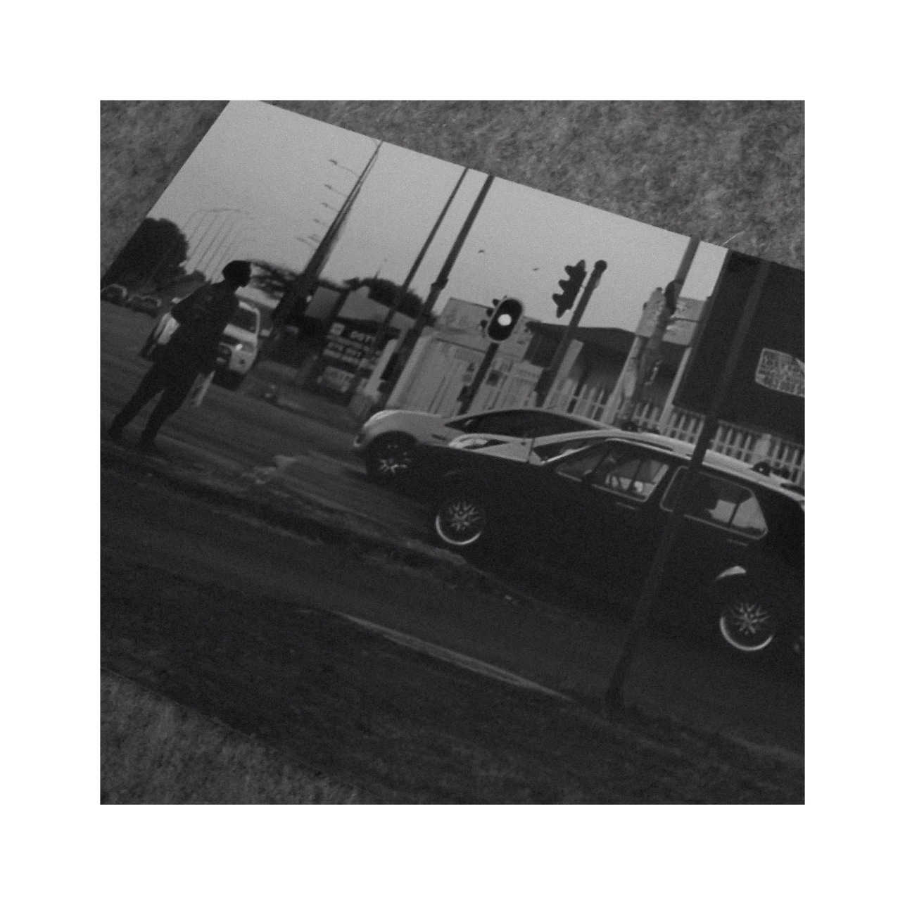 A photo of a photo. A newspaper selling between cars at a traffic intersection.