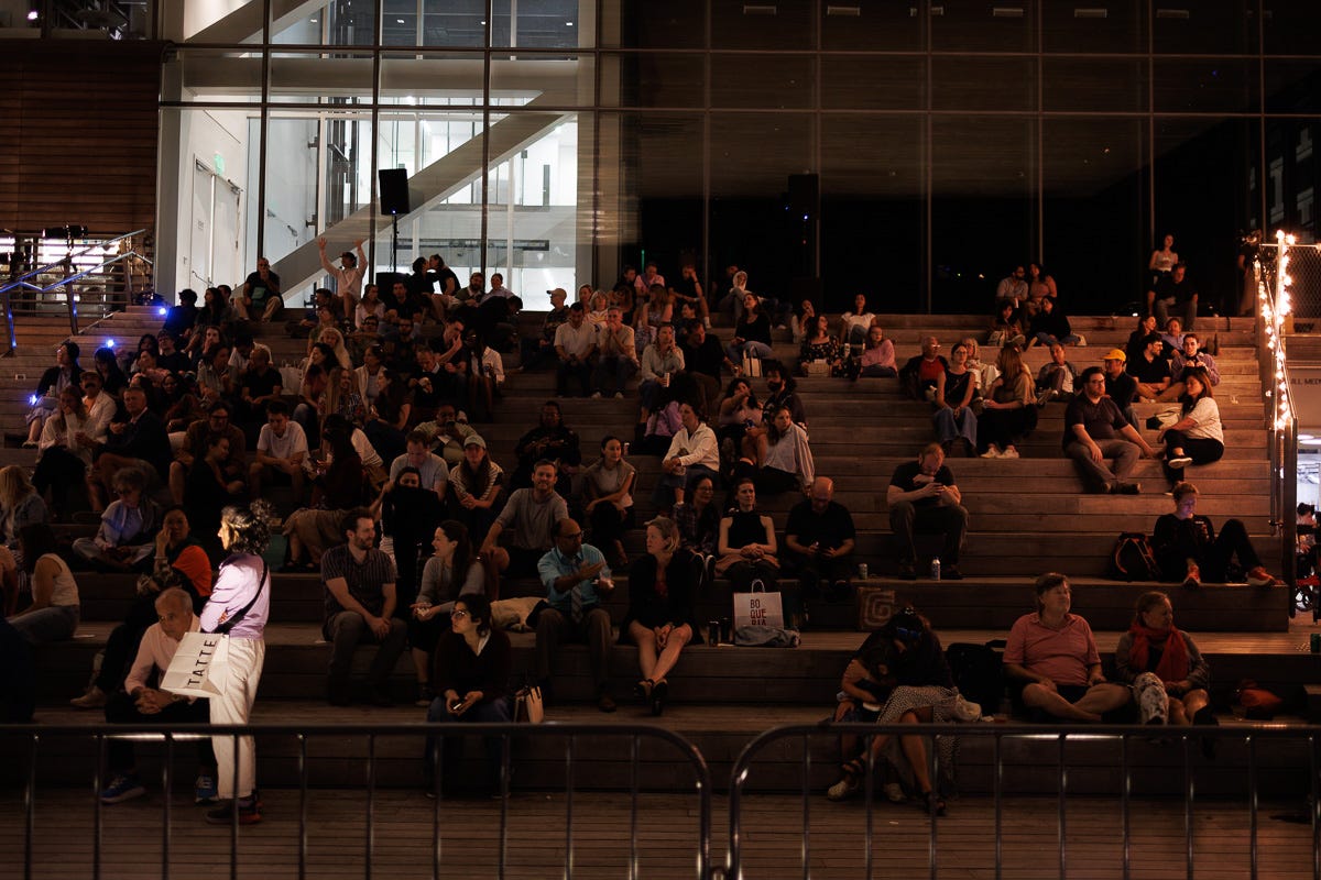 Large group of people seated on outdoor steps at night outside ICA in Boston Seaport