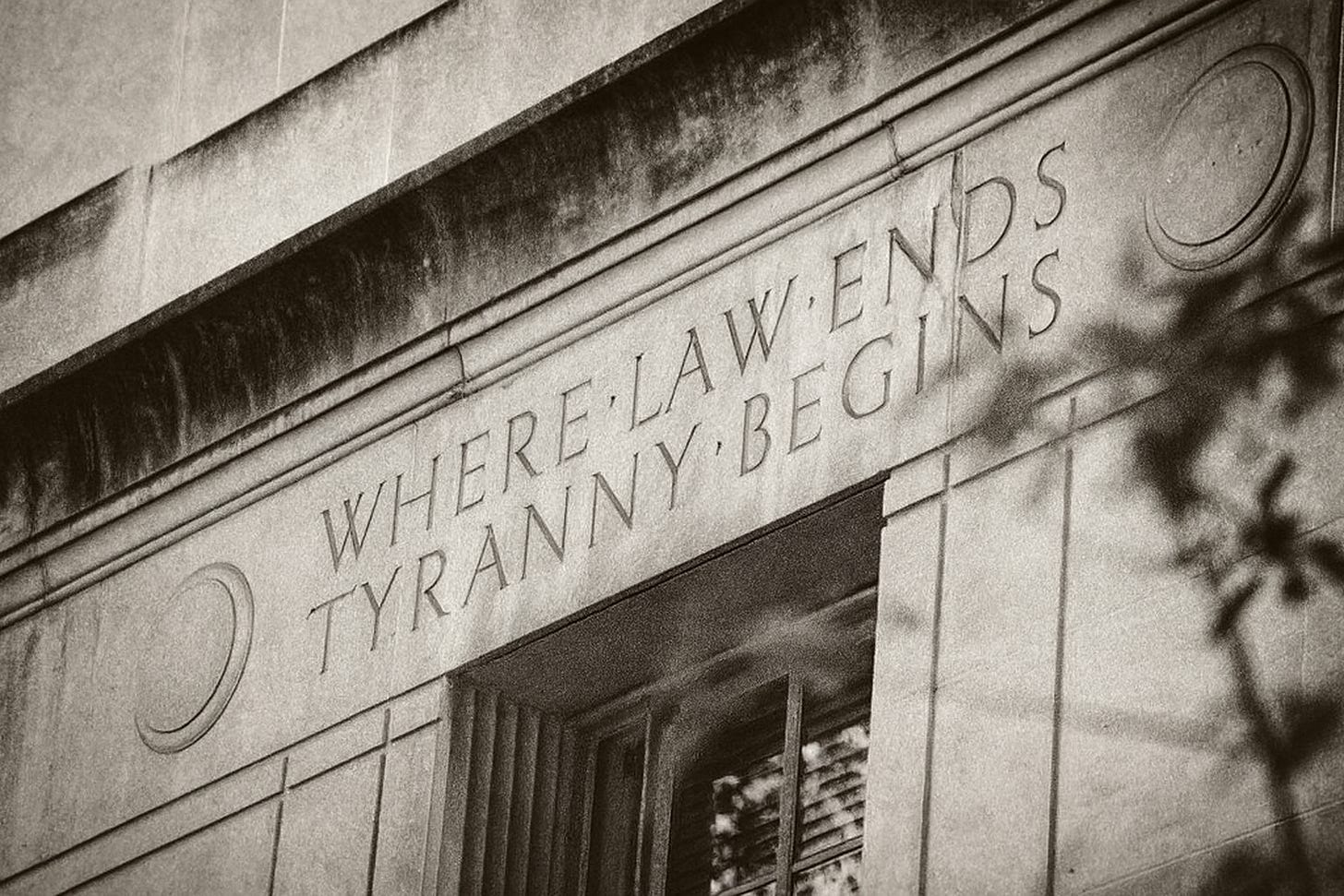 Black-and-white photograph of the Department of Justice building inscription reading ‘Where Law Ends Tyranny Begins,’ referencing the essay ‘At the End of the Law Is Tyranny’ and symbolizing the fragility of lawful democracy.
