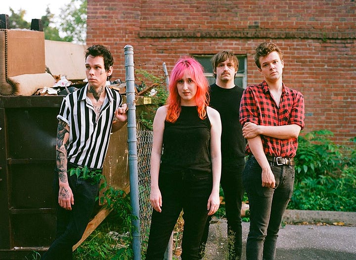 First image is a person with blonde hair surrounded by greenery and shadows. Second image is a group of four people standing together. Third image is of a person wearing glasses and playing guitar on a stage. Fourth image is of five people hugging in front of a wooded area. 