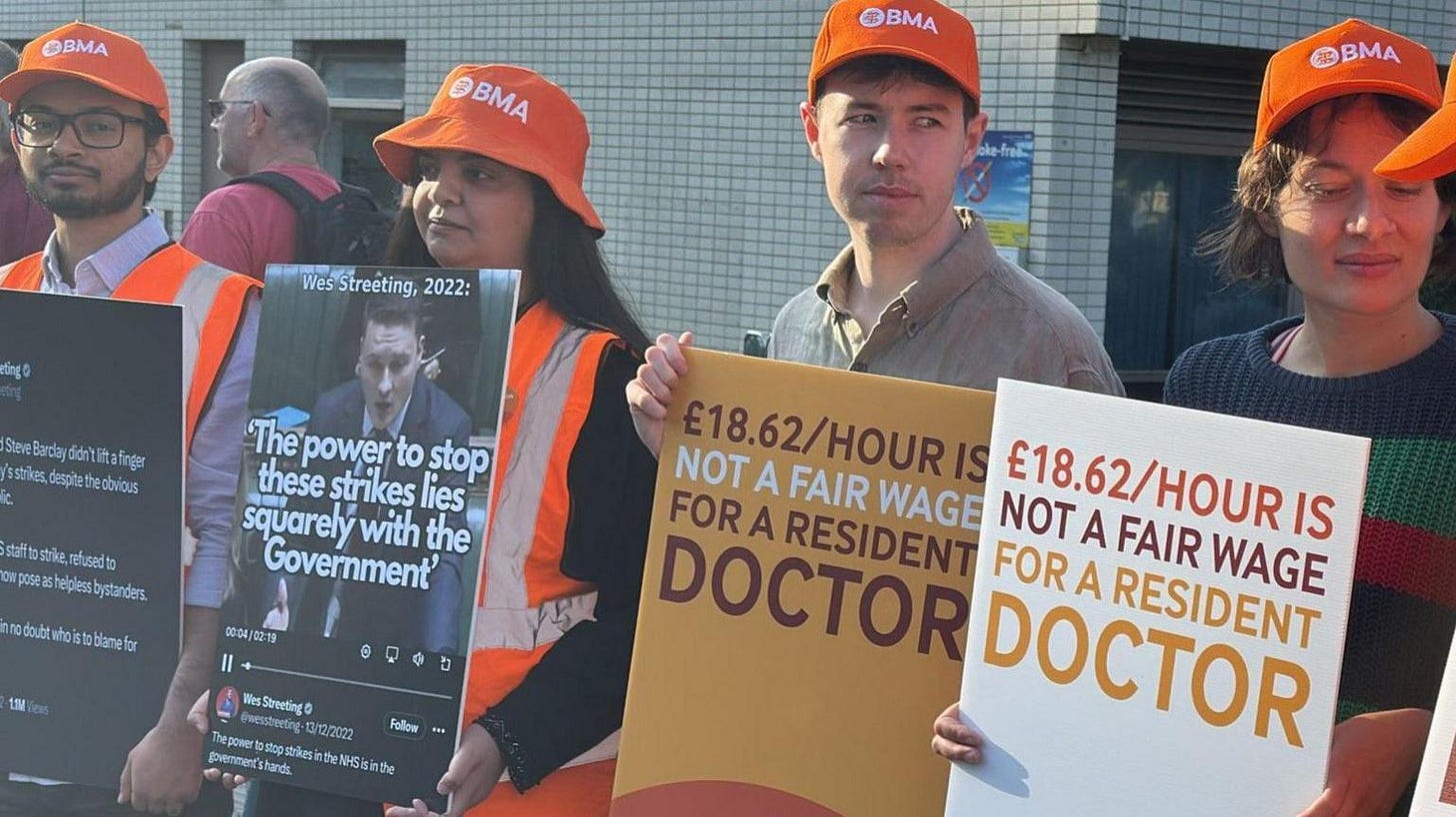 Striking doctors on a picket line. they are holding signs and wearing orange hats.
