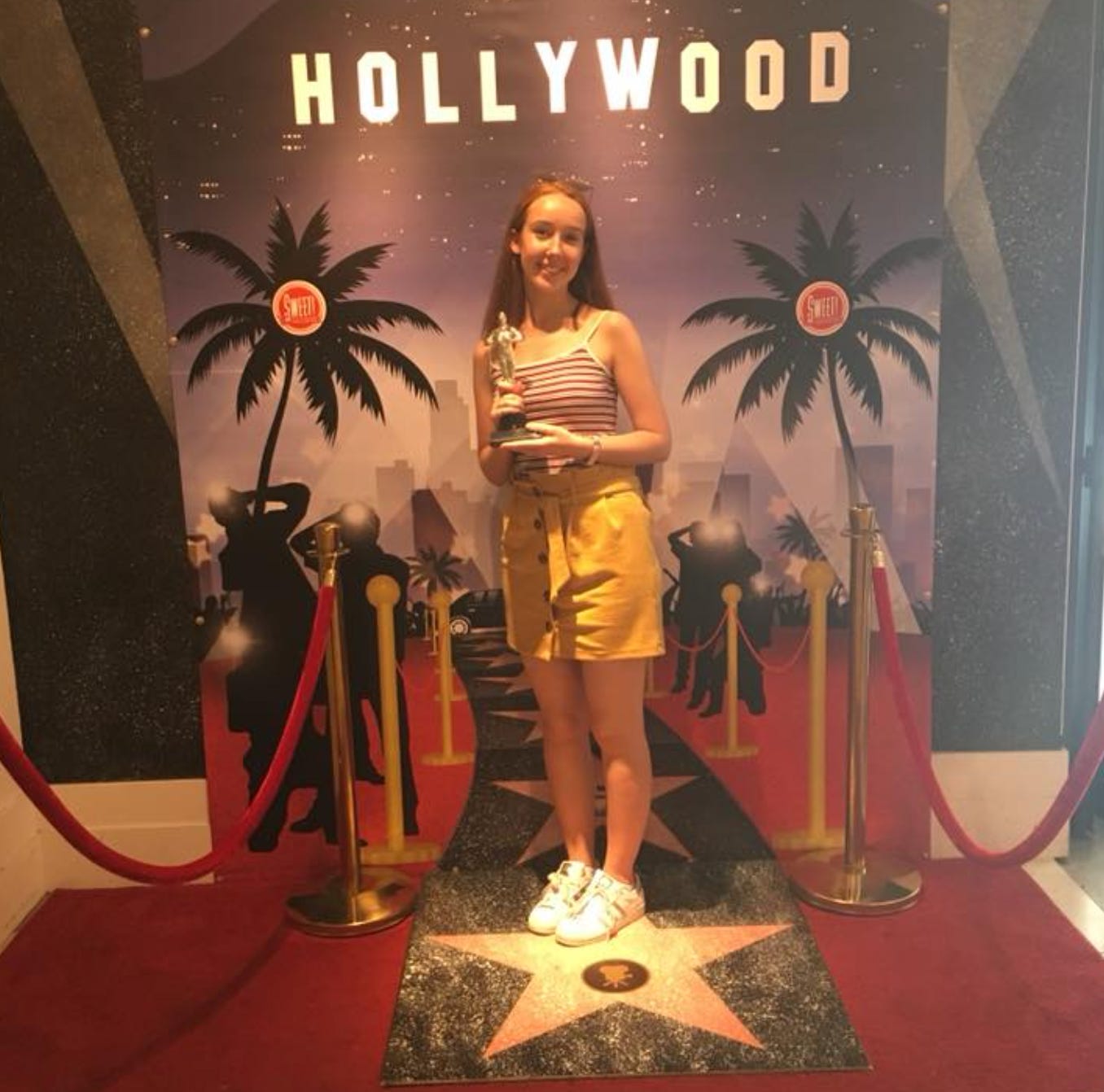 Girl holding a fake oscar in front of a fake Hollywood sign