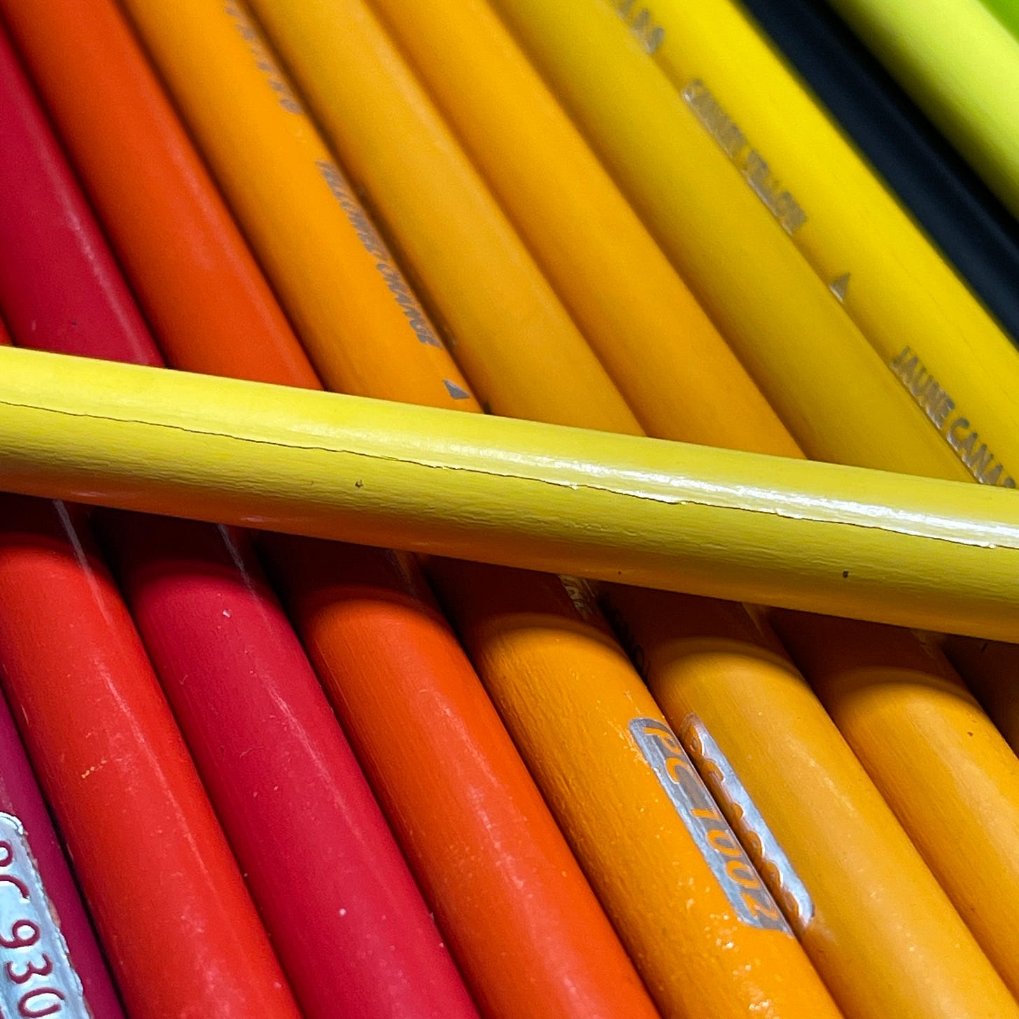 orange, red, and yellow colored pencils with one yellow pencil showing a large crack along its side
