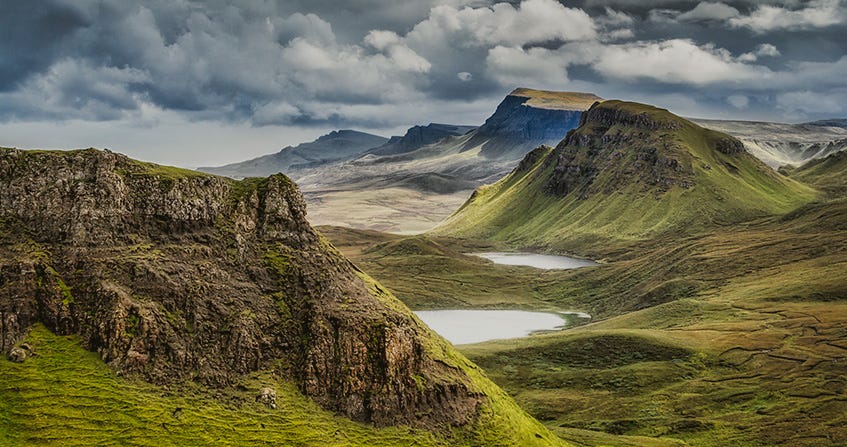 Craggy moss green hills and cliffsides, wiht a cloudy grey sky above
