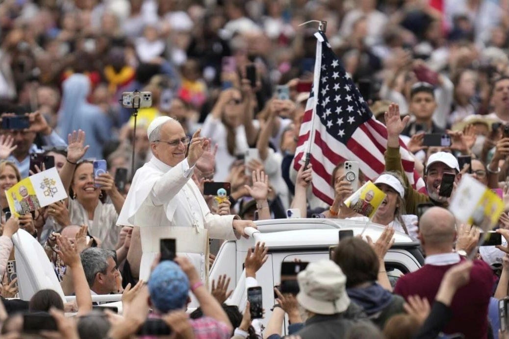 Pope Leo XIV waves from the popemobile beside an American flag