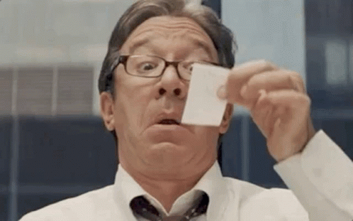a man wearing glasses is holding a piece of paper in front of his face .