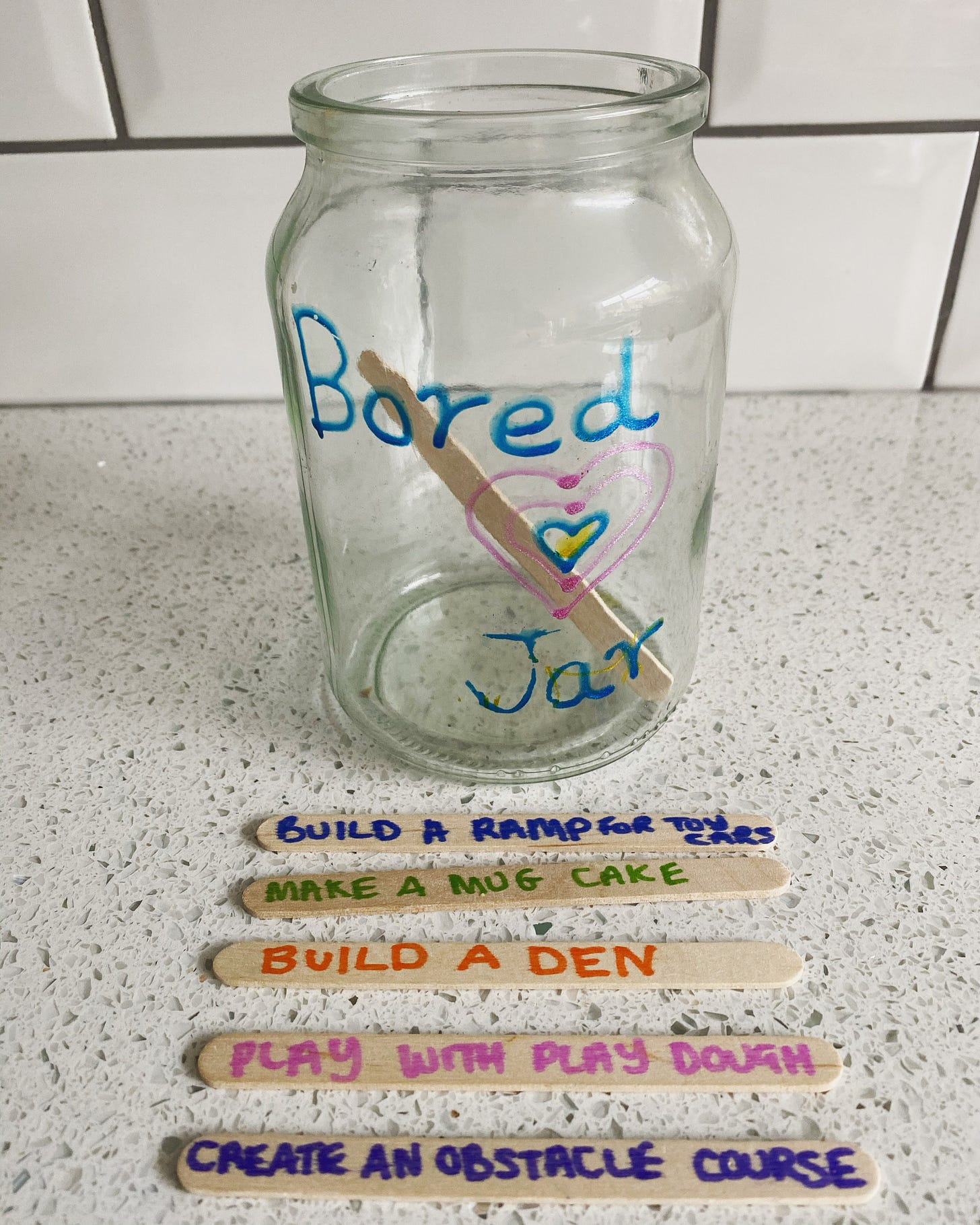Glass jar with write on 'Bored Jar' in front there are lolipop sticks with activities written on
