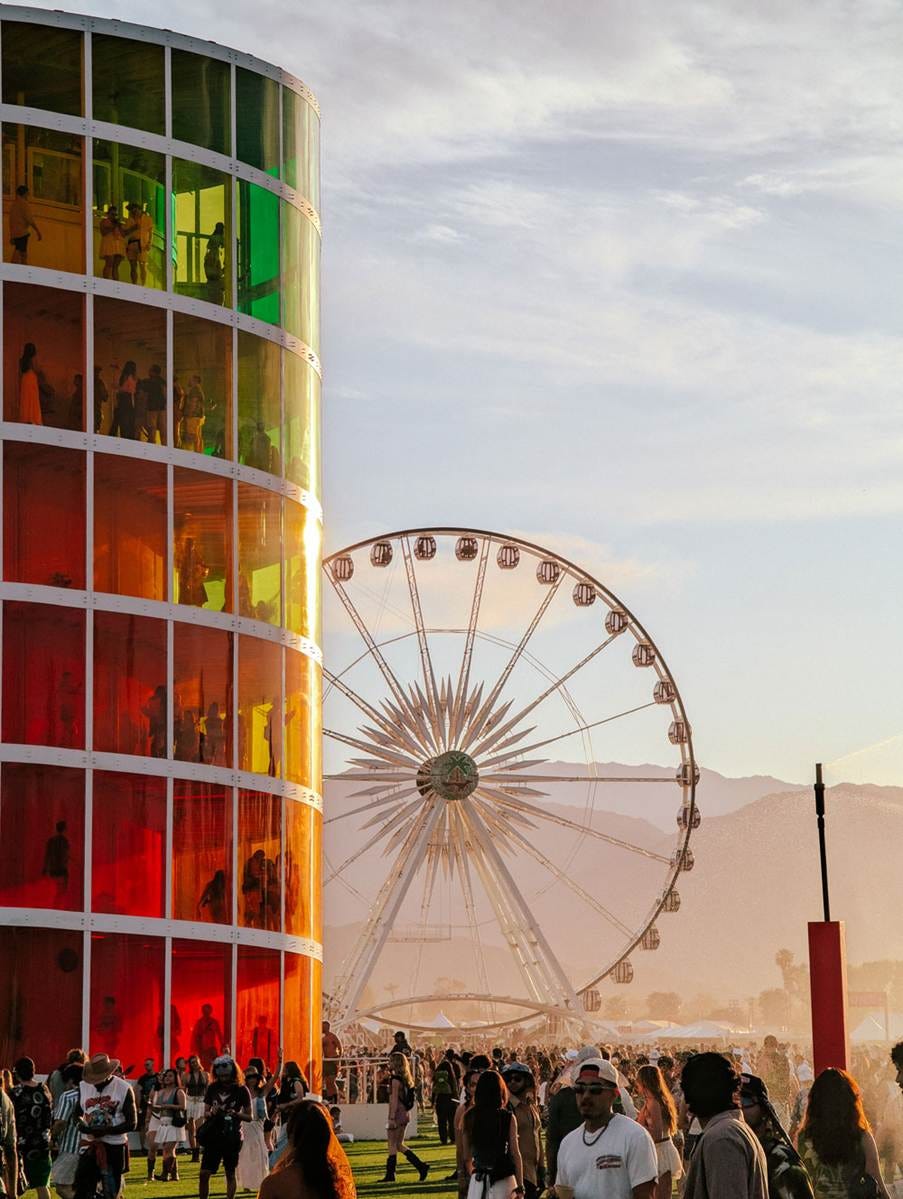 A lively outdoor festival scene with installations, Ferris wheel and people in summer clothes enjoying an event.