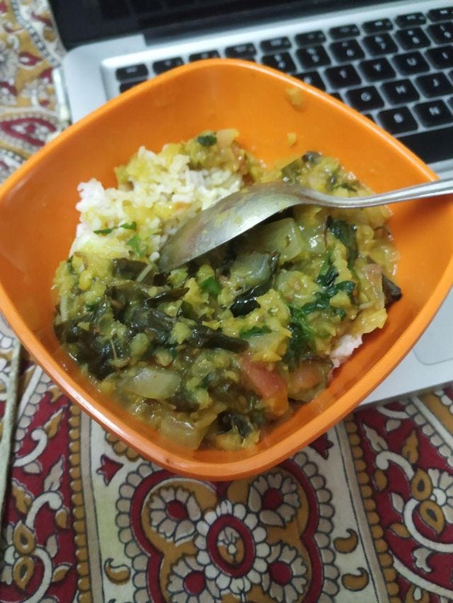 An orange bowl of dal and rice placed on top of a computer.