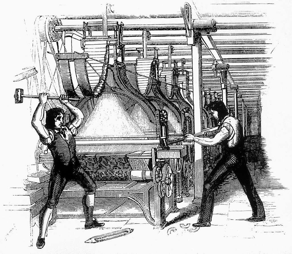 A 19th-century black and white engraving showing two figures using hammers to destroy a large textile frame. The machinery dominates the scene; the two figures stand on either side, mid-swing.