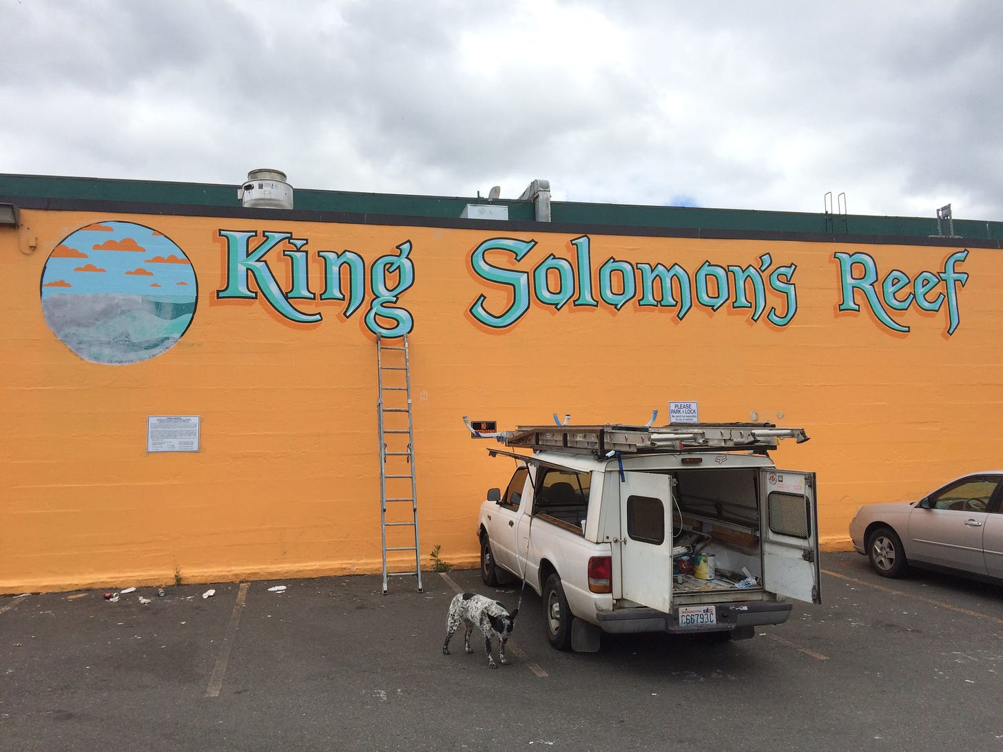 Painter's truck, ladder, and dog in front of the sherbet-orange wall of King Solomon's Reef, with lettering and design in blue