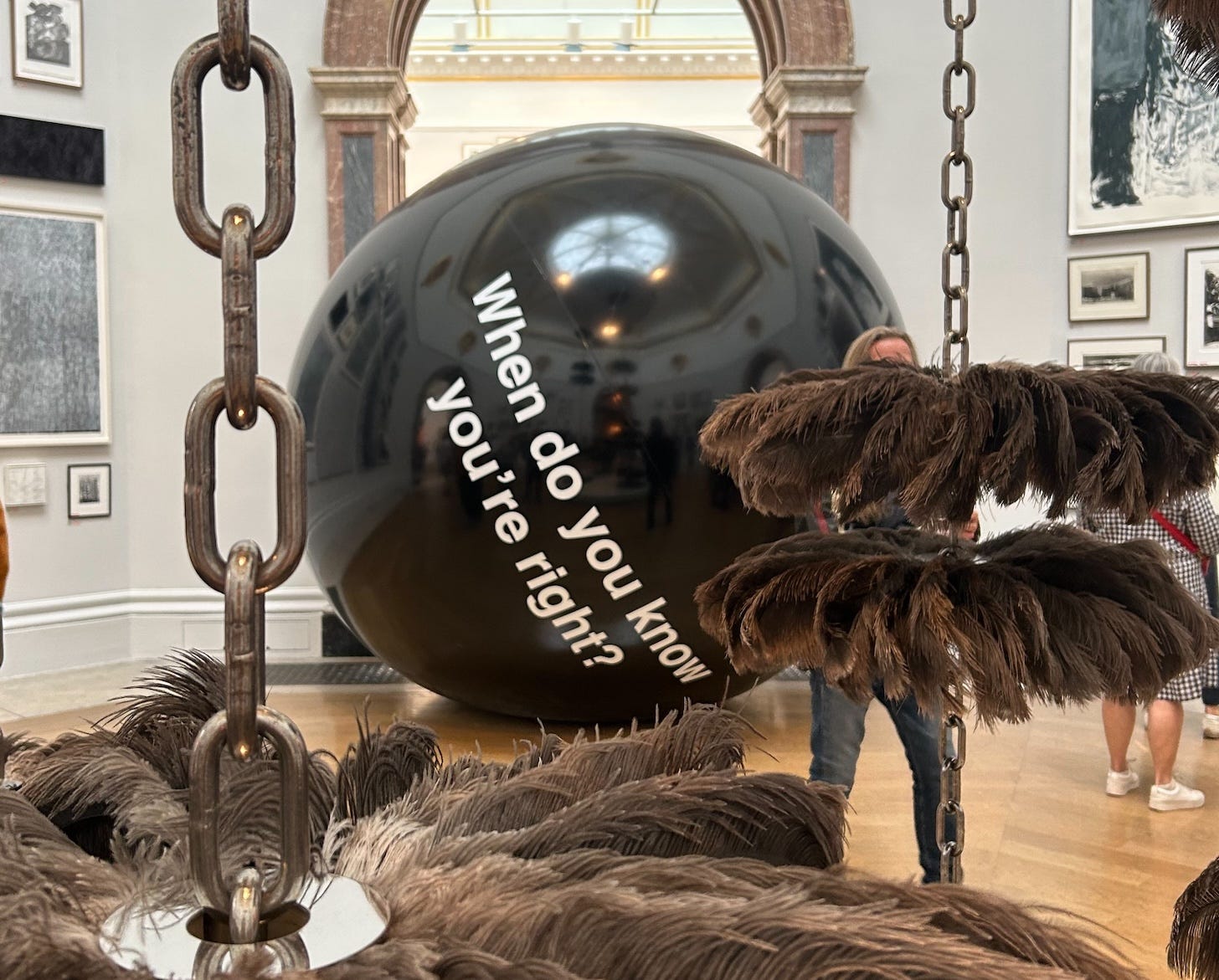 At the Royal Academy Summer Exhibition 2025. Showing two works of sculpture. The first, by Ryan Gander RA, WHEN DO YOU KNOW YOU’RE RIGHT?, made from Pvc and ink, with dimensions 300 x 300 x 300 cm. The second by Alice Channer, BODY SHOP, made from Ostrich feather, car body cleaning discs, stainless steel chains, and mirror-polished and lazer-cut stainless steel with dimensions 640 x 300 x 300 cm.