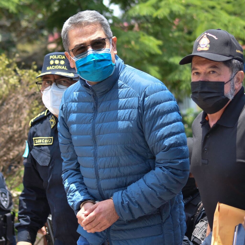 Juan Orlando Hernández, wearing handcuffs and a face mask, is being escorted by police officers.