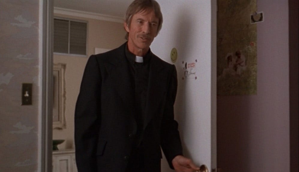 Father Moody in the threshold, looking down and frame-right.