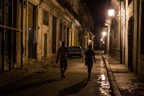 A 3x3 grid of nine photographs depicting life in Cuba. Images include: a boy diving into water; children sitting by a wall; flamingos in a lake; colorful colonial street scenes with classic cars and horse-drawn carts; a cat and a dog in a window; and a lamp-lit cobblestone street at night.