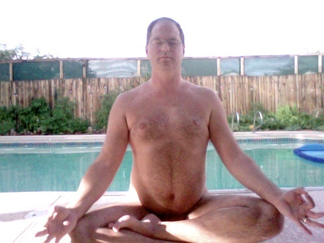 Dan Speers sits nude in a cross‑legged meditation pose at the edge of an outdoor swimming pool, eyes closed and hands resting on his knees. Behind him is a wooden fence lined with greenery, and soft afternoon light casts gentle shadows across the scene. Dan Speers sits nude in a cross‑legged meditation pose at the edge of an outdoor swimming pool, eyes closed and hands resting on his knees. Behind him is a wooden fence lined with greenery, and soft afternoon light casts gentle shadows across the scene.