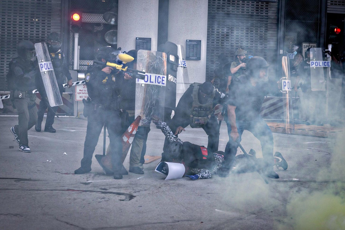 Department of Homeland Security police arrest a demonstrator outside the Metropolitan Detention Center amid smoke.