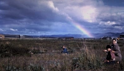 Unalakleet, Alaska, when the sky is saturated with clouds and a bright rainbow. People are living their lives under the backdrop of the sky.