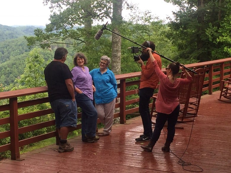 three people stand before a man with a camera and a woman with a large boom microphone to film an interview