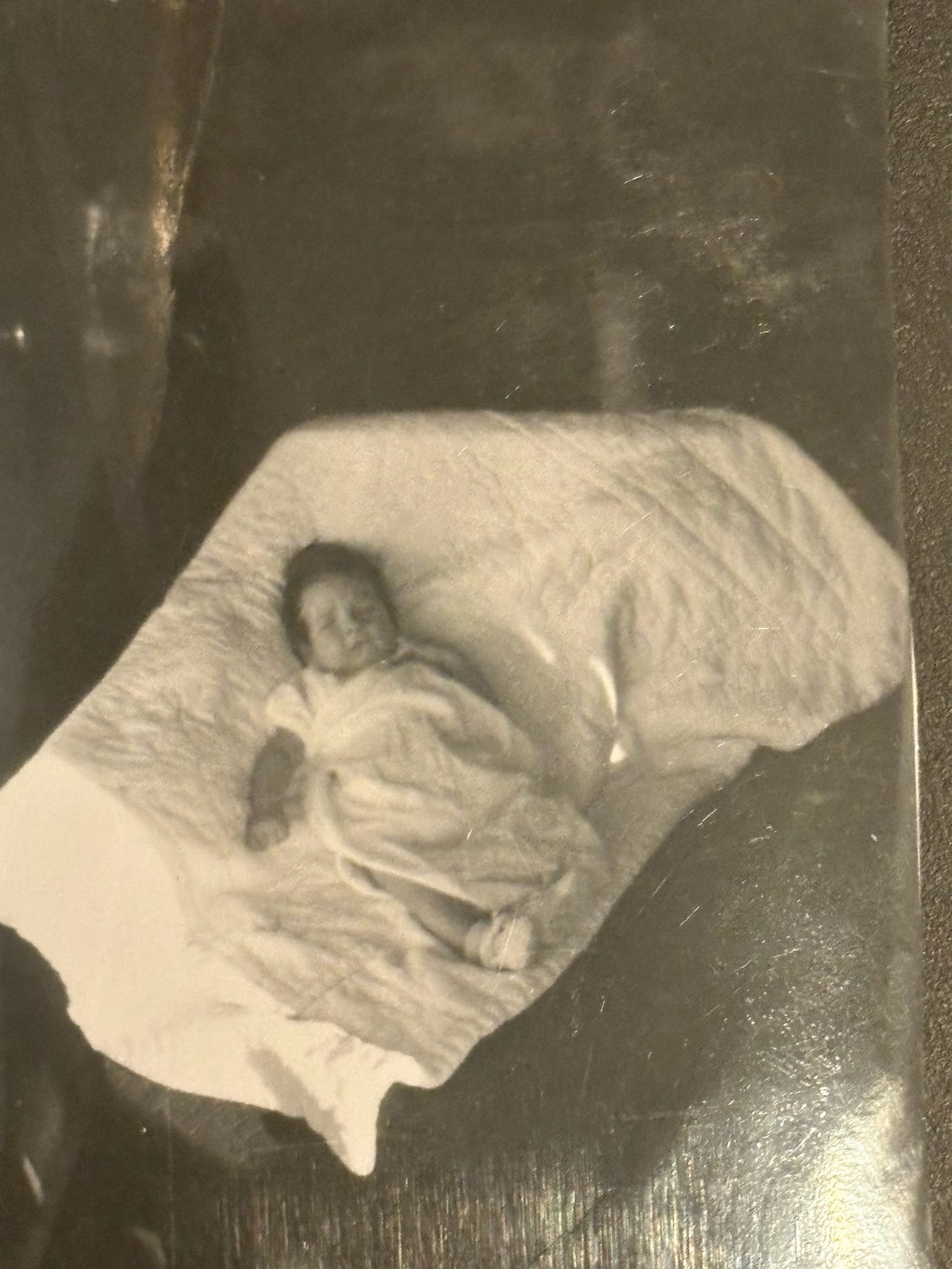 A black and white photo of a baby wrapped in a white blanket on top of another white blanket.