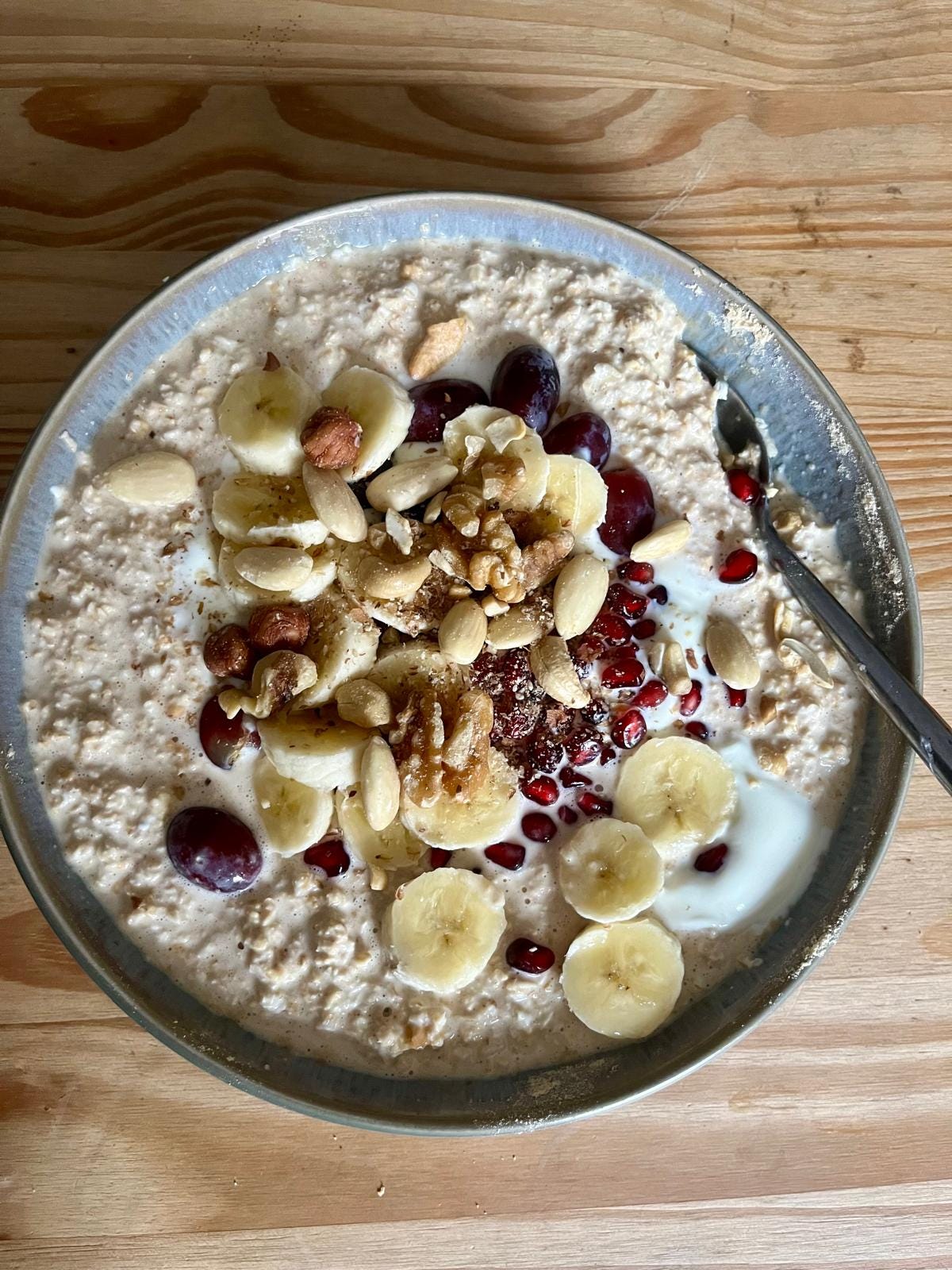 A bowl of fermented oats topped with bananas, grapes, seeds, walnuts, almonds, and yogurt.