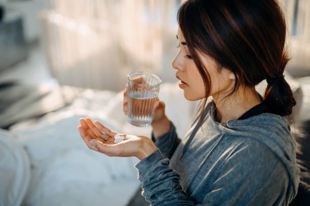 Young Asian woman sitting on bed and feeling sick, taking medicines in hand with a glass of water Young Asian woman sitting on bed and feeling sick, taking medicines in hand with a glass of water Depression treatment stock pictures, royalty-free photos & images