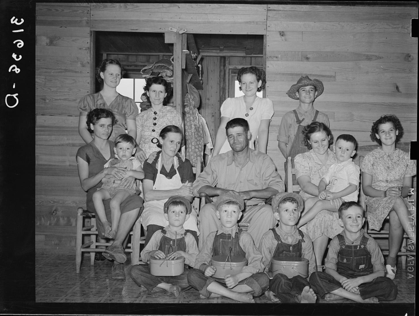 A black and white photo shows a family of 15, smiling at the photographer. A black and white photo shows a family of 15, smiling at the photographer.