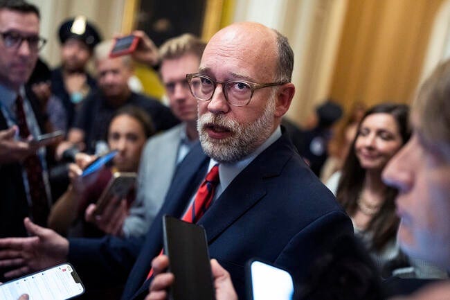 Office of Management and Budget Director Russell Vought, a white man with a white beard and a mostly bald head, wearing a business suit and glasses, talks with reporters after attending the Republican Senate luncheon in the U.S. Capitol.
