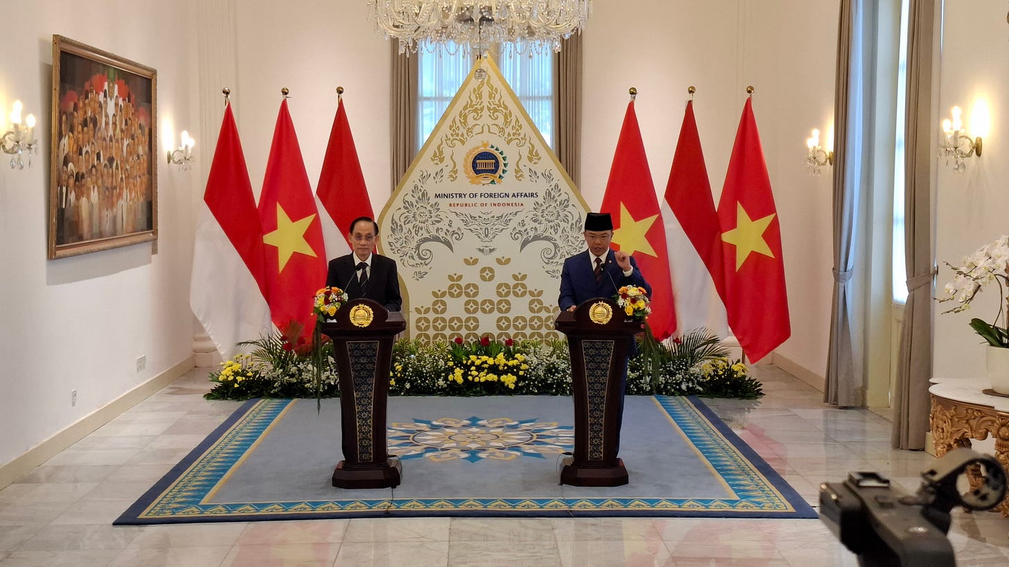 Two officials in formal attire stand at separate wooden podiums during a press conference at the Ministry of Foreign Affairs of the Republic of Indonesia, flanked by the national flags of Indonesia and Vietnam. Two officials in formal attire stand at separate wooden podiums during a press conference at the Ministry of Foreign Affairs of the Republic of Indonesia, flanked by the national flags of Indonesia and Vietnam.