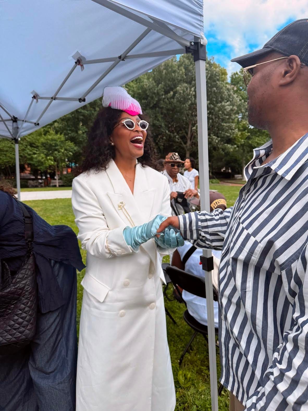a joyful person in a white suit coat, pink hat and light blue satin gloves greets a participant in a procession a joyful person in a white suit coat, pink hat and light blue satin gloves greets a participant in a procession