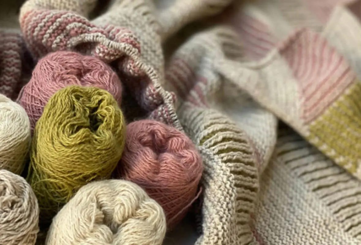 five yarn cakes, three off-white, two pink and one green, and knitted striped shawl