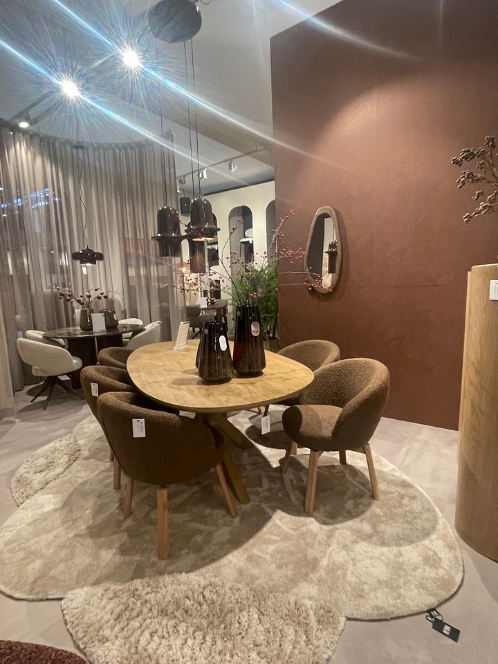 Dining table vignette at Maison & Objet Paris 2026 featuring sculptural pendant lighting, neutral textured walls, artisan tableware, and soft contemporary seating. Modern dining furniture display at Maison & Objet Paris 2026 showcasing upholstered chairs, round wood table, warm earth-tone palette, and layered lighting design.