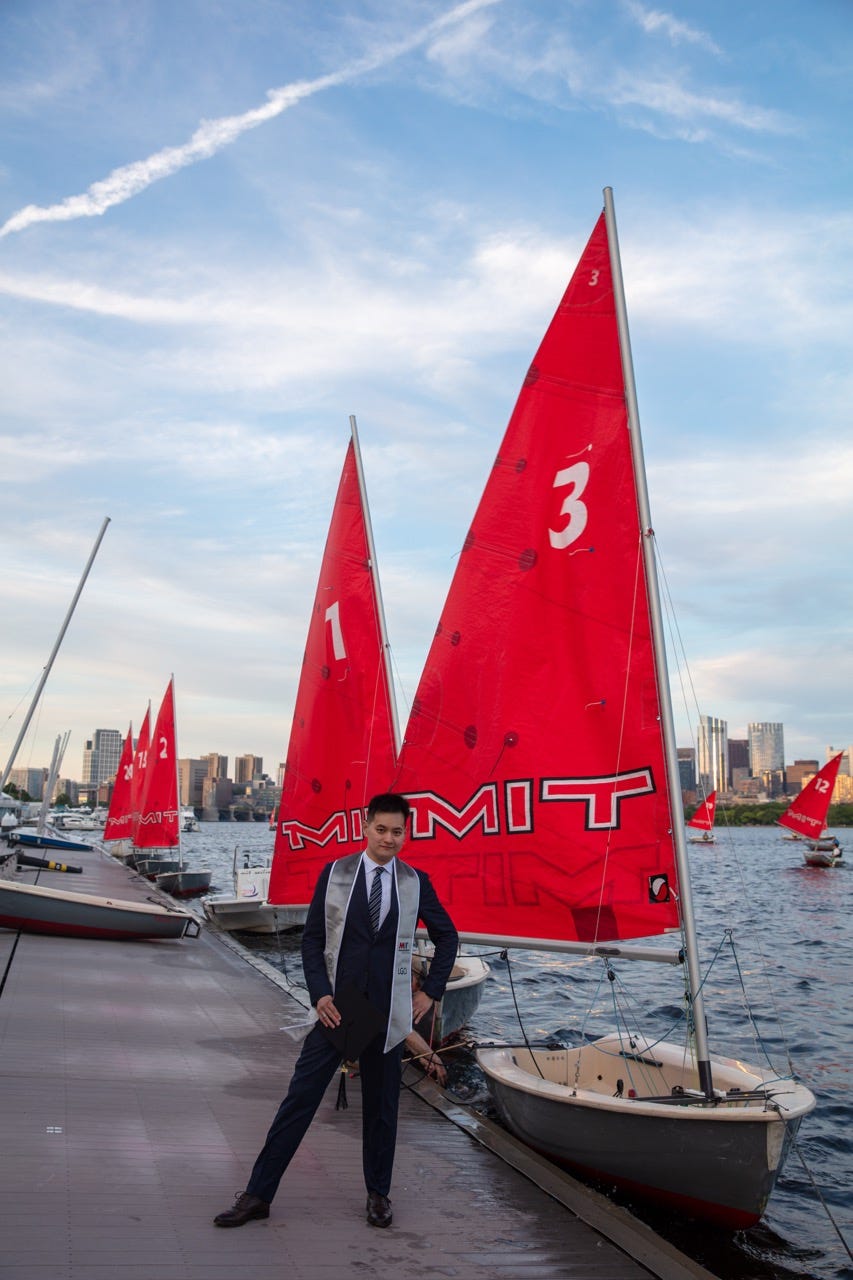 Junru in a suit and LGO graduation stole standing beside a docked MIT dinghy on the Charles River Junru in a suit and LGO graduation stole standing beside a docked MIT dinghy on the Charles River