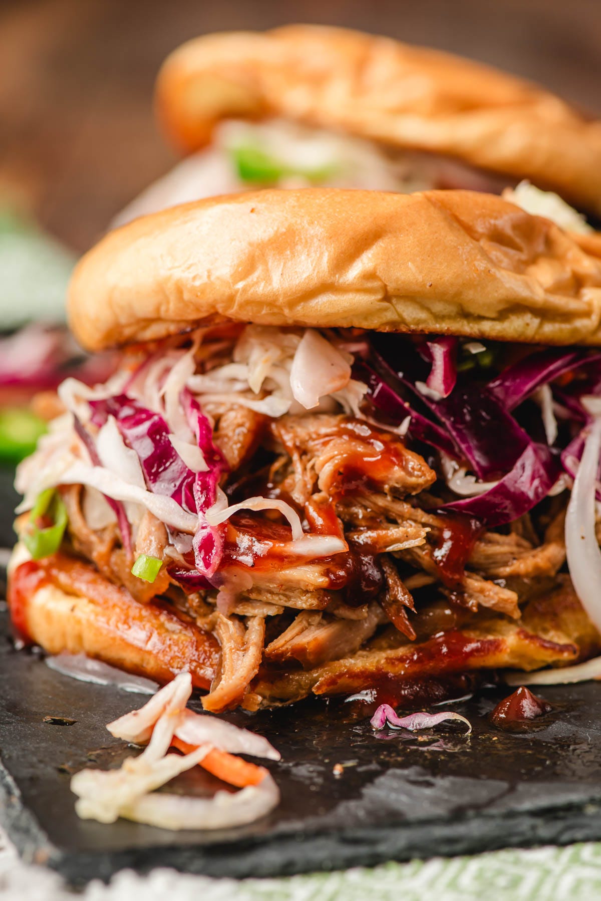 A spicy pulled pork sandwich topped with coleslaw and BBQ sauce on a brioche bun.