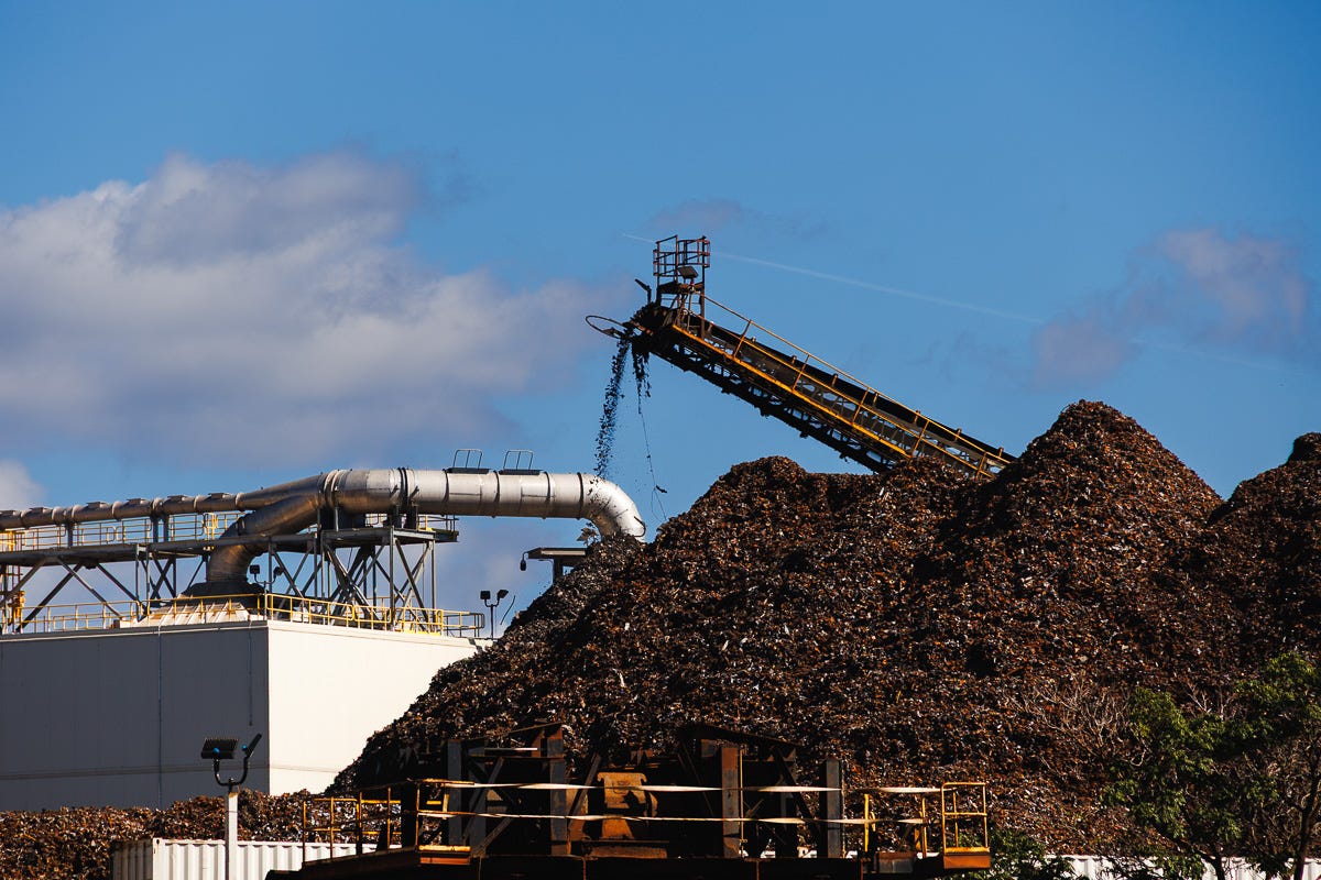 Close view of conveyor dropping shredded metal onto large scrap piles near industrial pipes in Boston Harbor Close view of conveyor dropping shredded metal onto large scrap piles near industrial pipes in Boston Harbor