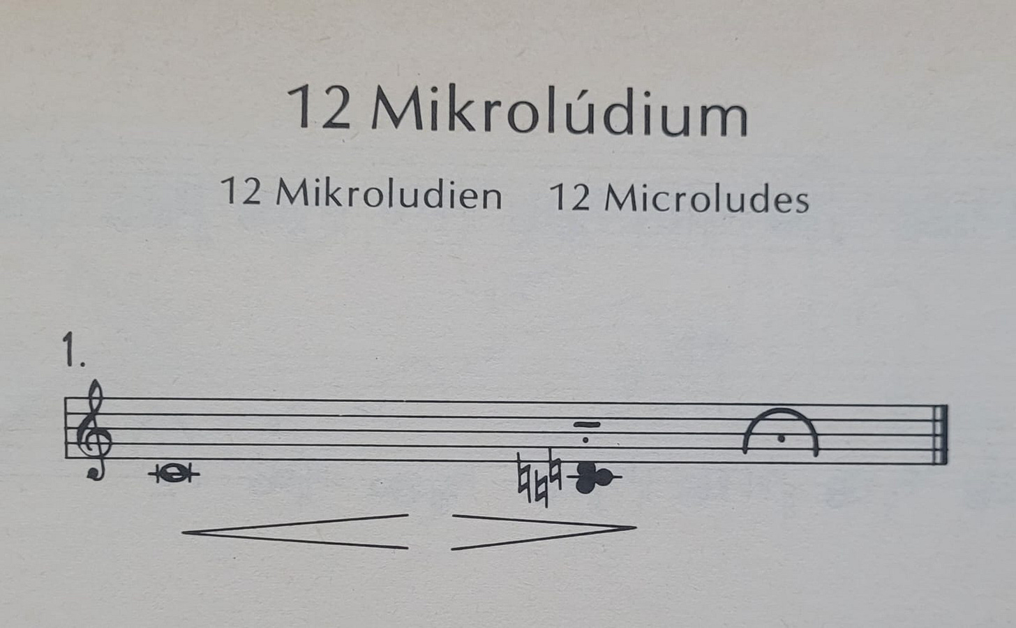 The score for the first of the 12 Microludes by György Kurtág: two notes, a middle C followed by a B-C-D cluster. There is a crescendo-decrescendo indication underneath the held C. The score for the first of the 12 Microludes by György Kurtág: two notes, a middle C followed by a B-C-D cluster. There is a crescendo-decrescendo indication underneath the held C.