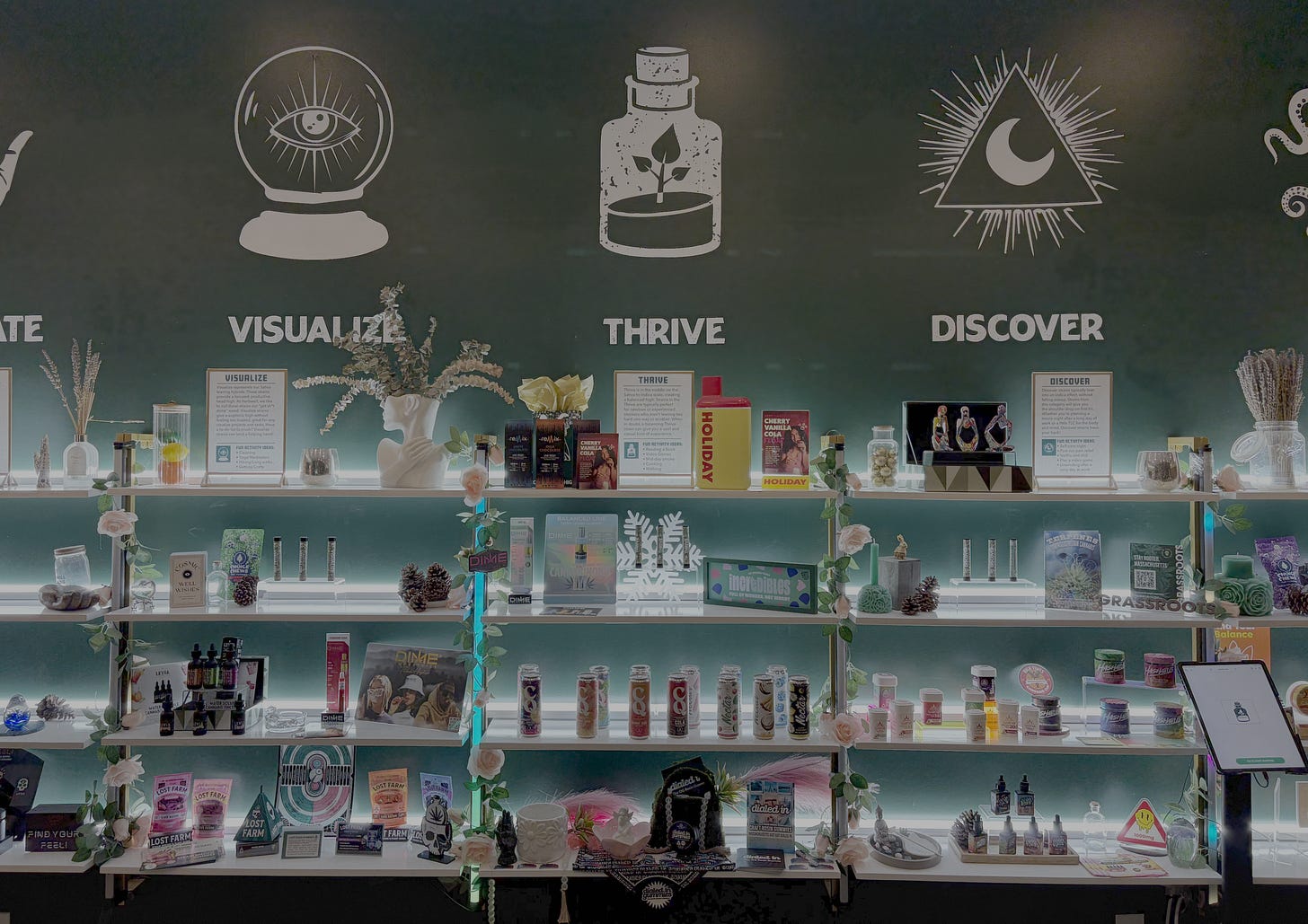 Colorful cannabis products are displayed on shelves. The wall behind has a large, graphic which says "Levitate, Visualize, Thrive, Discover." Colorful cannabis products are displayed on shelves. The wall behind has a large, graphic which says "Levitate, Visualize, Thrive, Discover."