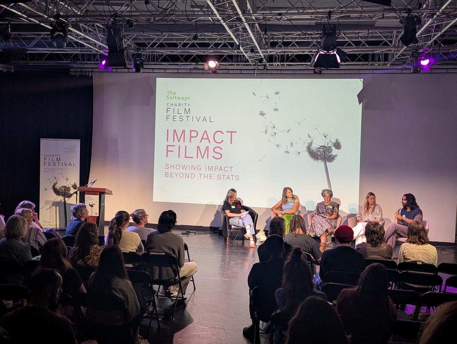 An auditorium with people sitting on chairs looking at a panel discussion. An auditorium with people sitting on chairs looking at a panel discussion.