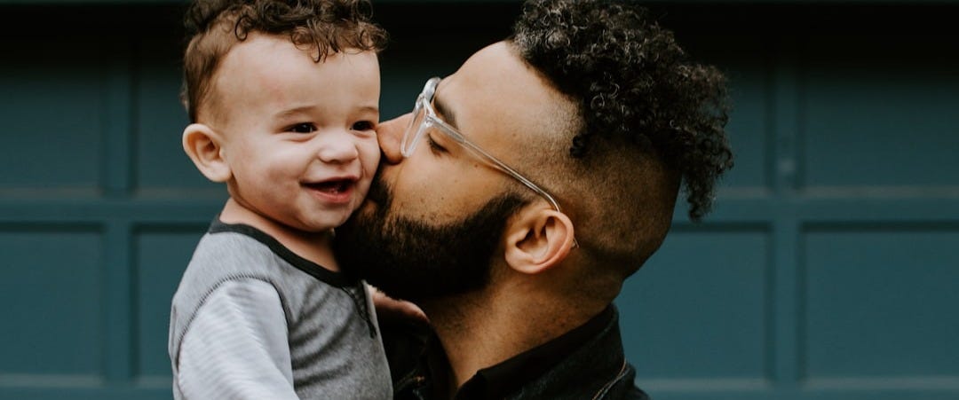 man carrying baby boy and kissing on cheek