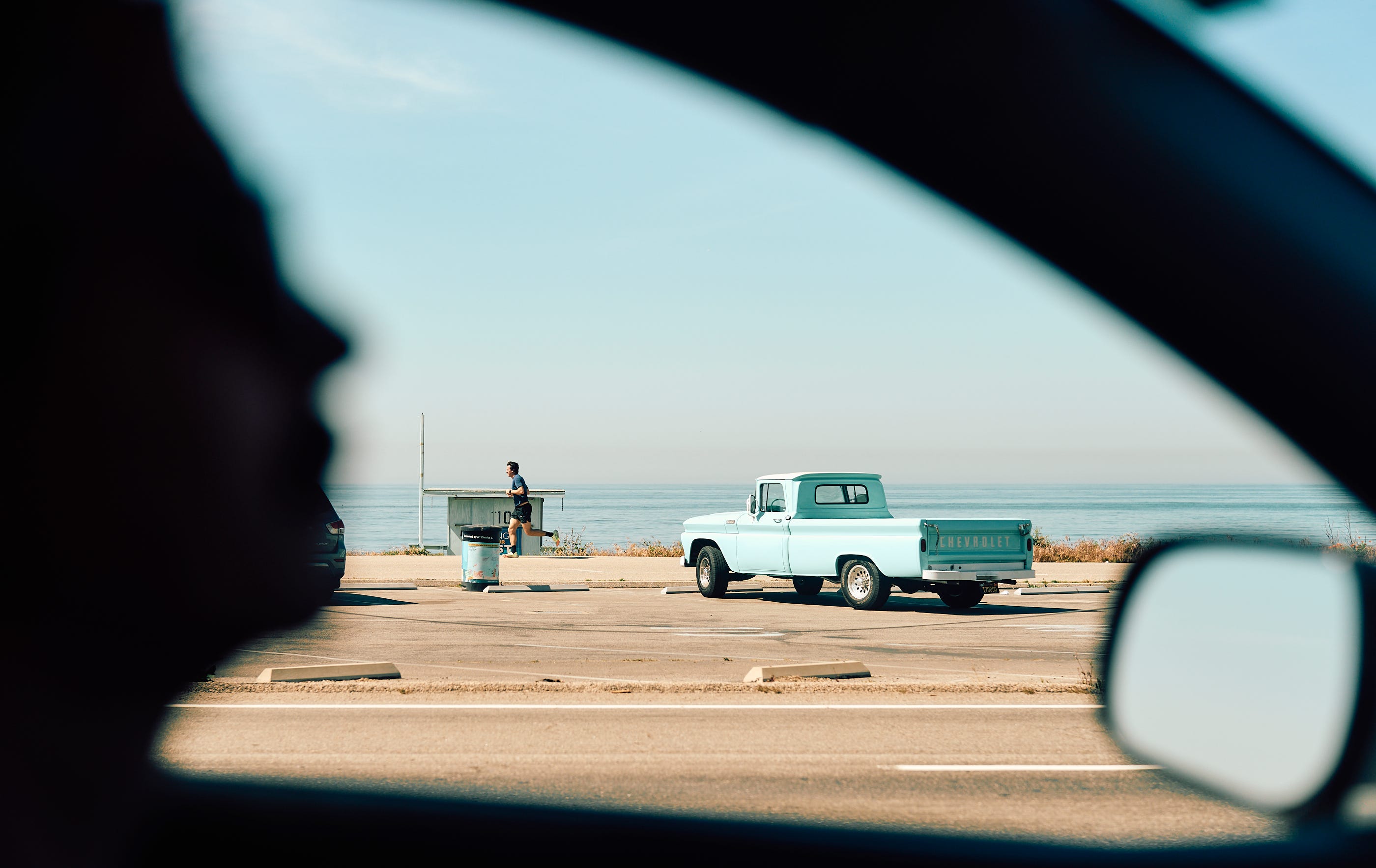 Silhouetted driver on the PCH with the Pacific Ocean, the beach, a jogger and a vintage pickup truck in the background