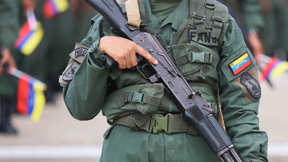 Color photograph of the torso of a Venezuelan soldier holding a gun downward across their body