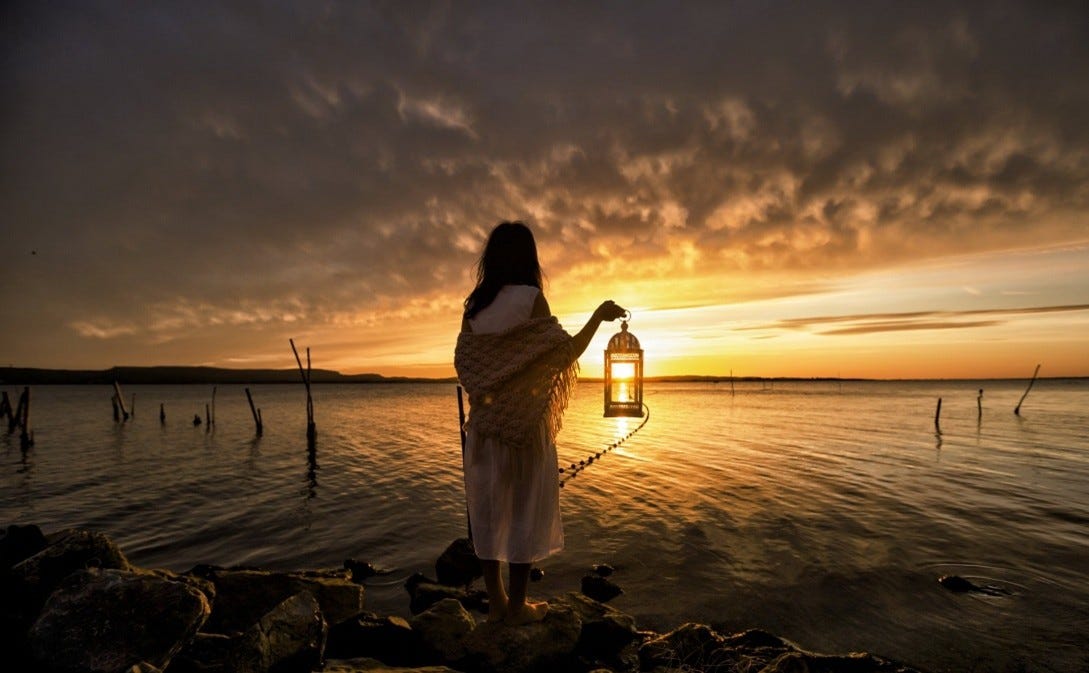 A woman walks at sunset, lantern in hand — symbolizing the search for lost selfhood.