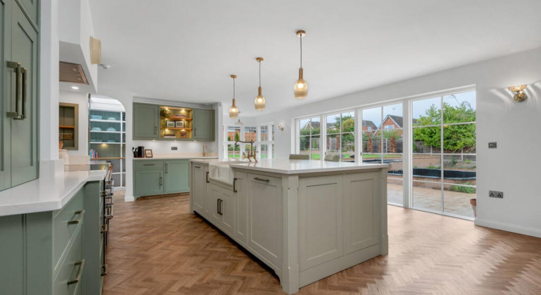 A kitchen with green cabinetry, a kitchen island, white walls, and pendant lights A kitchen with green cabinetry, a kitchen island, white walls, and pendant lights
