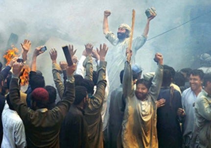 Group of islamic men in traditional clothing raising their arms and cheering, with smoke and fire in the background.