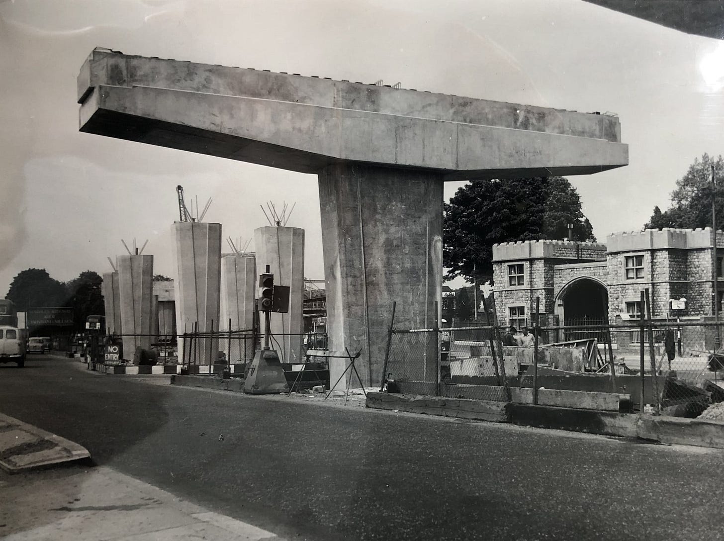 Black and white photograph of the M4 viaduct at Brentford under construction. One concrete pillar in the centre of the frame supports a wide T-shaped cross beam; a series of other pillars have also been built in the distance with reinforcement bars sticking out of the top. Black and white photograph of the M4 viaduct at Brentford under construction. One concrete pillar in the centre of the frame supports a wide T-shaped cross beam; a series of other pillars have also been built in the distance with reinforcement bars sticking out of the top.