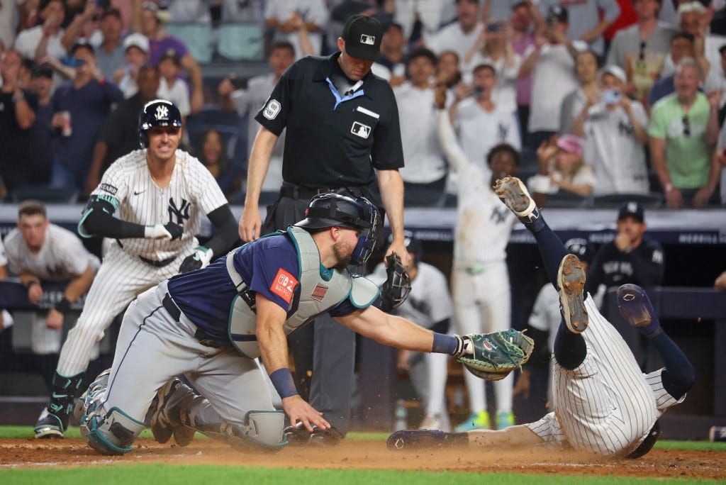 Anthony Volpe eludes the tag of Cal Raleigh dives safely to score the game-winning run in the 10th-inning of the Yankees' comeback win over the Mariners.