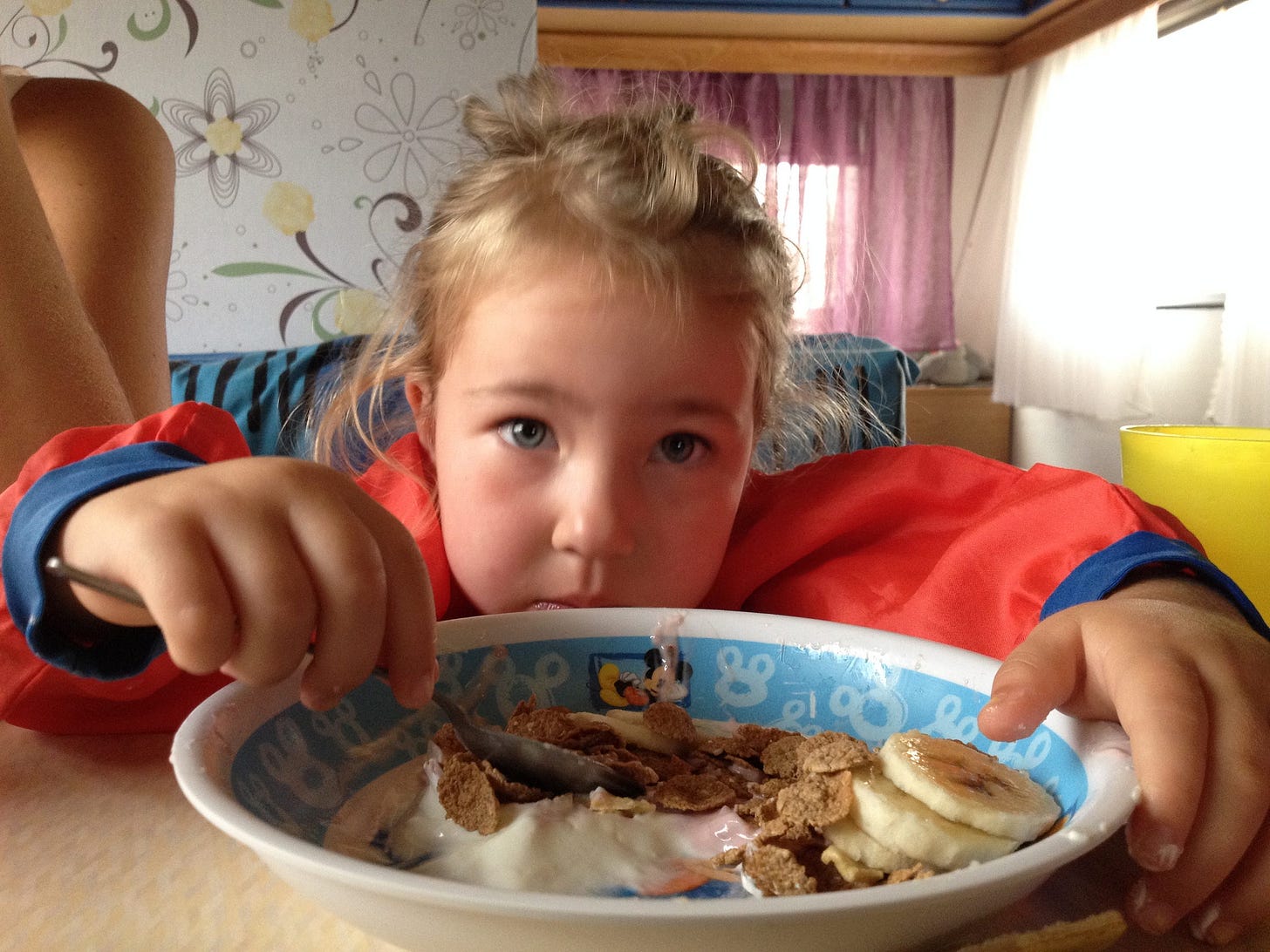 A young child enjoying a bowl of cereal, yogurt and bananas